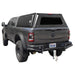 Image of a dark grey RAM pickup truck with a black truck bed cap installed. The cap has a rear window and a side access door, shown from a rear three-quarter view on a white background