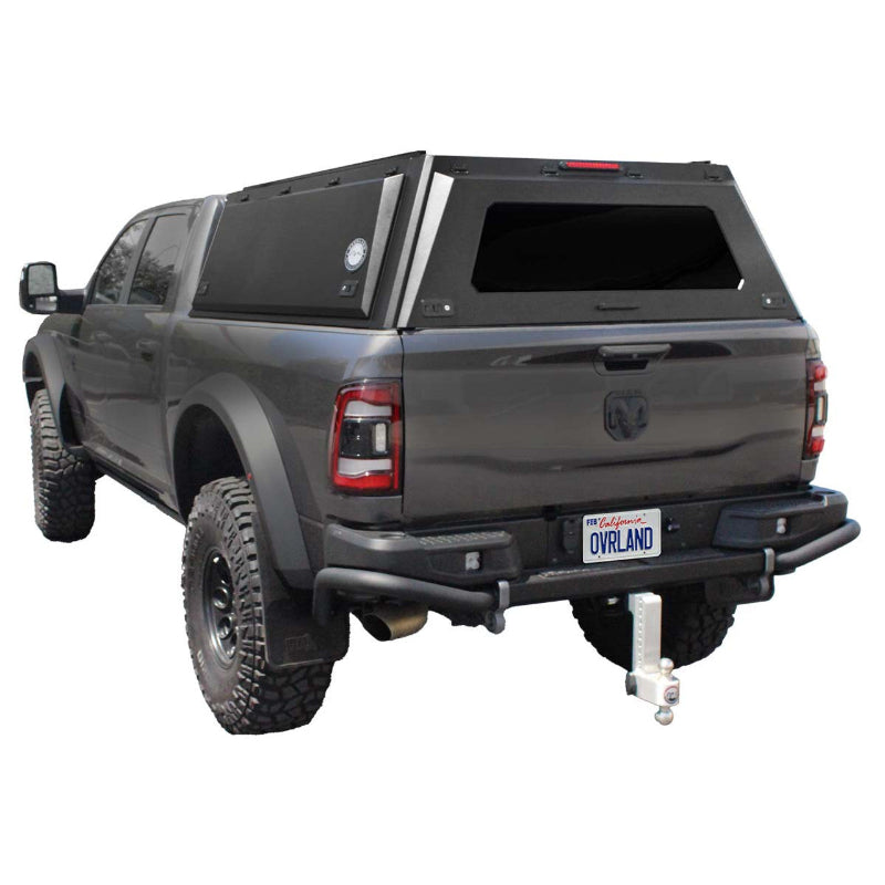 Image of a dark grey RAM pickup truck with a black truck bed cap installed. The cap has a rear window and a side access door, shown from a rear three-quarter view on a white background