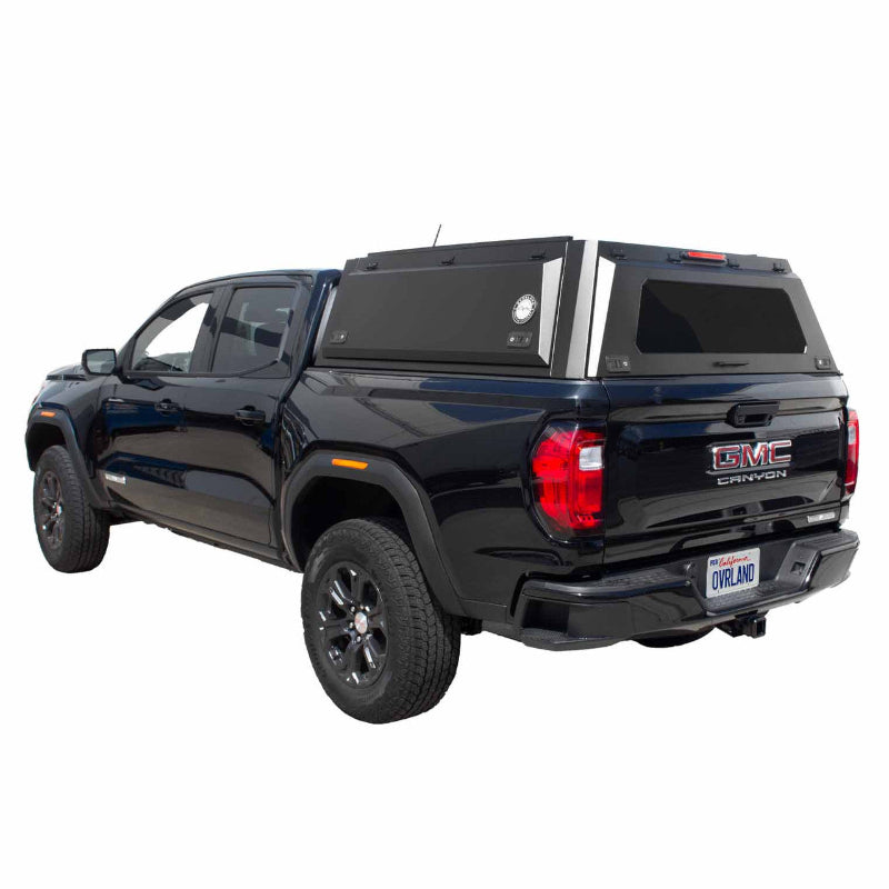 Image of a black GMC Canyon truck with a black truck bed cap installed. The cap has a rear window and side access doors, shown from a rear three-quarter perspective on a white background