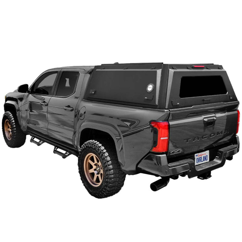 Image of a grey Toyota Tacoma truck with a black truck bed cap installed. The cap has a rear window and side access doors, shown from a rear three-quarter view on a white background