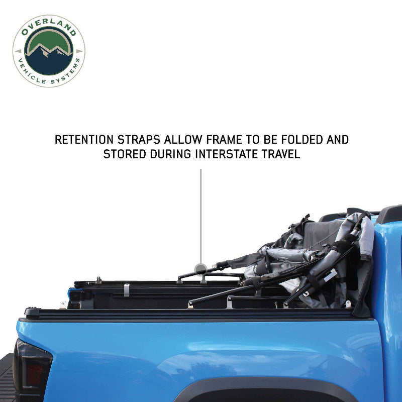 Image of a blue pickup truck with the soft shell camper top folded and stored, angled side view on a white background. The text "RETENTION STRAPS ALLOW FRAME TO BE FOLDED AND STORED DURING INTERSTATE TRAVEL" is visible above the truck bed