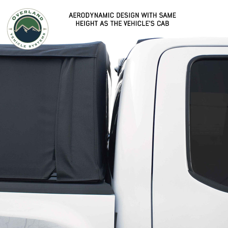 Image showing the height of a black soft shell camper top relative to the cab of a white pickup truck, close-up side view on a white background. Text reads "AERODYNAMIC DESIGN WITH SAME HEIGHT AS THE VEHICLE'S CAB"