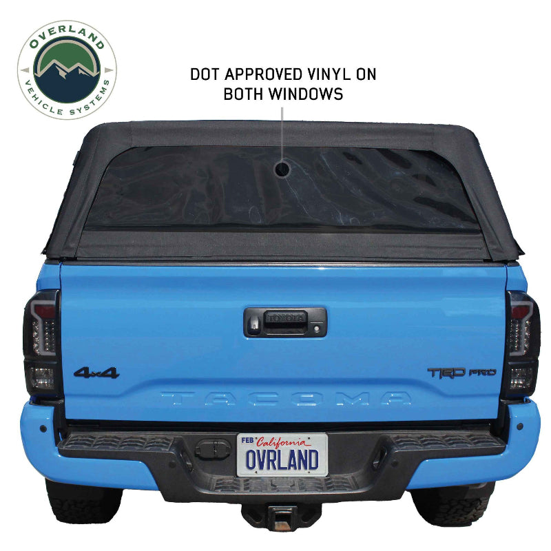 Image of an Overlanding Vehicle Systems Explorer Soft Shell bed topper on a blue Toyota Tacoma pickup truck, angled rear view. The soft shell topper is made of black diamond canvas and has a clear vinyl rear window
