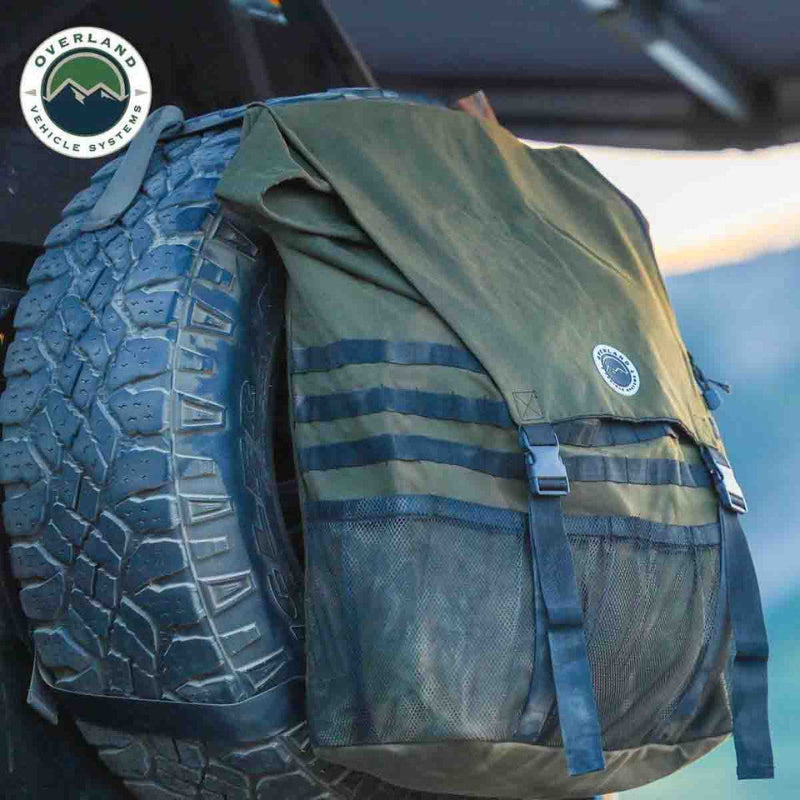 Image of a green and black backpack attached to a vehicle's spare tire, with the Overland Vehicle Systems logo visible.