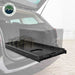 Image of an OVS black steel refrigerator slide extended from the back of a vehicle, with the cargo area of the vehicle visible, and a logo for "OVERLAND VEHICLE SYSTEMS" in the top left. This showcases the slide's practical application, making it easy to access items from the vehicle's rear