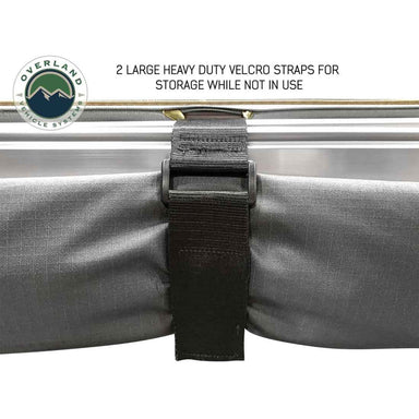 Image of a close-up on the Overland Vehicle Systems' Nomadic 180 Awning being secured for storage. A heavy-duty Velcro strap is wrapped around the folded gray awning fabric and aluminum frame to keep it in place