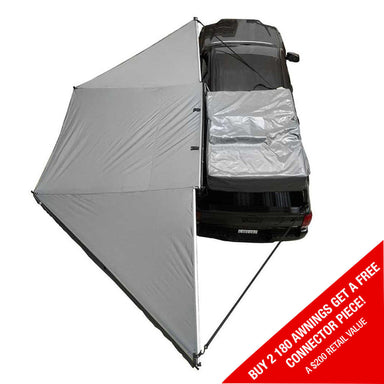 Image of OVS HD Nomadic 180 Degree Awning in dark grey with black travel cover, partially deployed on a vehicle, angled top view on white background