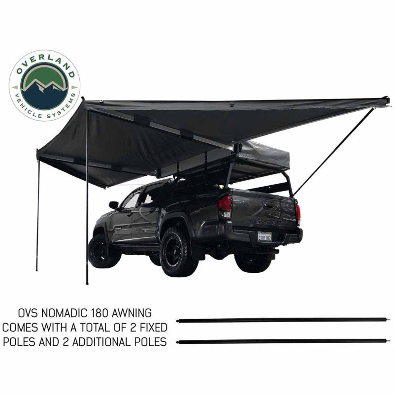 Image of the Overland Vehicle Systems' OVS Nomadic 180 Awning fully deployed on the rear and passenger side of a gray truck, supported by two fixed poles and two additional poles. The awning fabric is black and the frame is silver