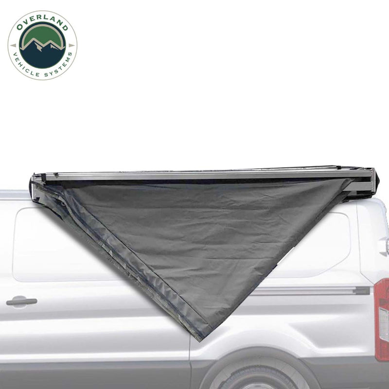 Image of the OVS Nomadic 180 Awning partially deployed on the side of a white van, showing the dark grey fabric rolled out in a triangular shape