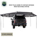Image of OVS HD Nomadic 180 awning connector kit 6-piece version with support poles deployed to increase wind resistance, light gray fabric extended around a pickup truck, rear view on a white background.