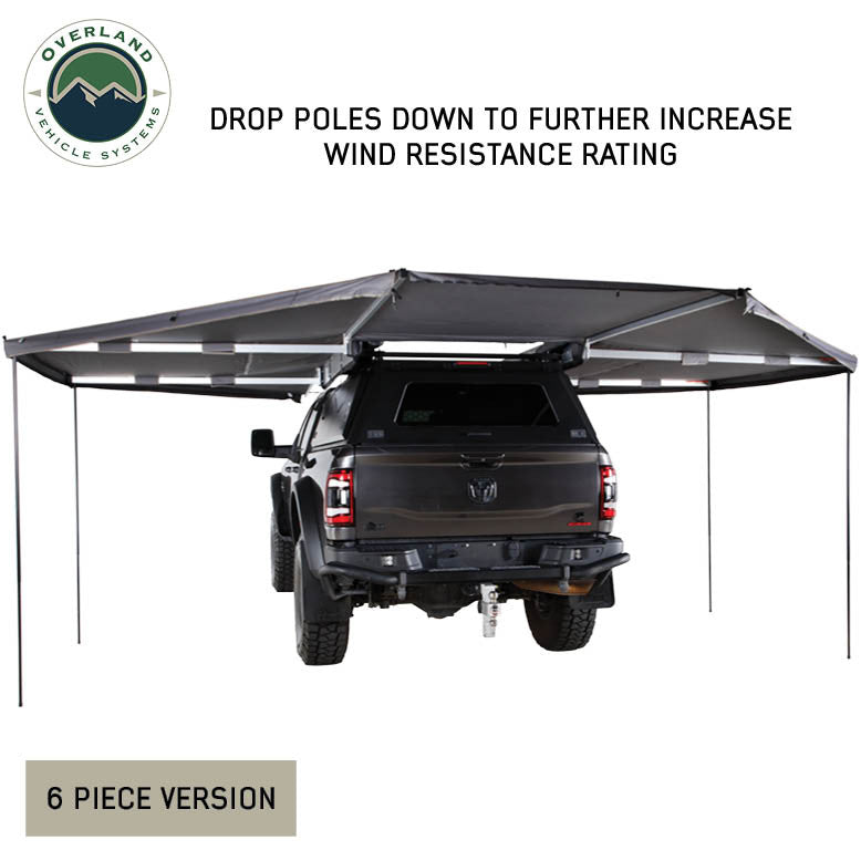 Image of OVS HD Nomadic 180 awning connector kit 6-piece version with support poles deployed to increase wind resistance, light gray fabric extended around a pickup truck, rear view on a white background.