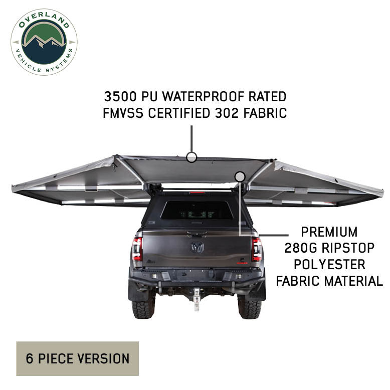 Image of OVS HD Nomadic 180 awning connector kit 6-piece version installed on a pickup truck, showing extended light gray ripstop fabric coverage with material callouts, rear view on a white background.