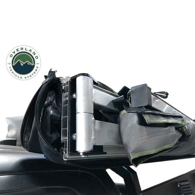 Image of a close-up of the heavy-duty aluminum hinge and hardware of an Overland Vehicle Systems 270-degree awning. The awning is partially unzipped from its black travel cover and mounted to a vehicle's rooftop, with the green awning fabric visible