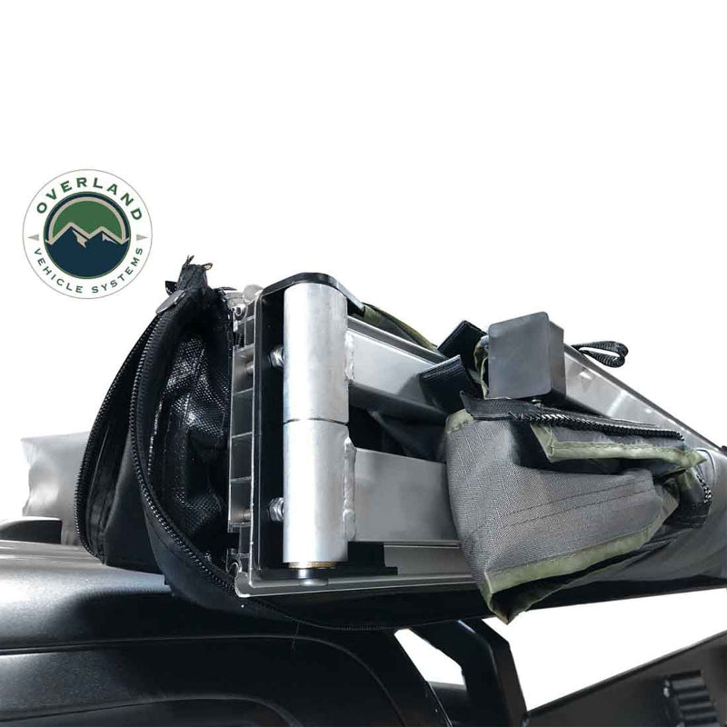 Image of a close-up of the heavy-duty aluminum hinge and hardware of an Overland Vehicle Systems 270-degree awning. The awning is partially unzipped from its black travel cover and mounted to a vehicle's rooftop, with the green awning fabric visible