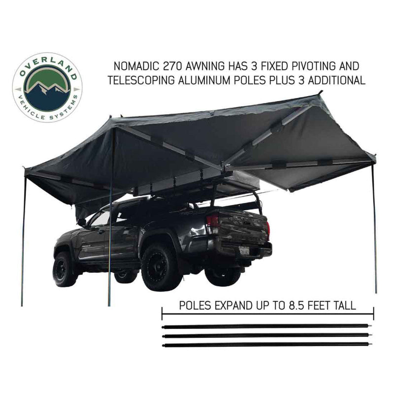 Image of an Overland Vehicle Systems Nomadic 270 awning, fully deployed from the side and back of a dark grey pickup truck. The grey awning fabric is supported by three fixed pivoting and telescoping aluminum poles, which expand up to 8.5 feet tall