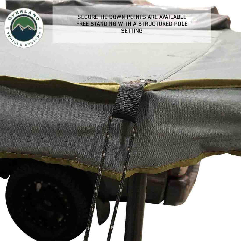 Image of a roof-mounted awning edge detail showing gray fabric canopy with reinforced tie-down point and cord for secure freestanding setup, close-up exterior view on white background.