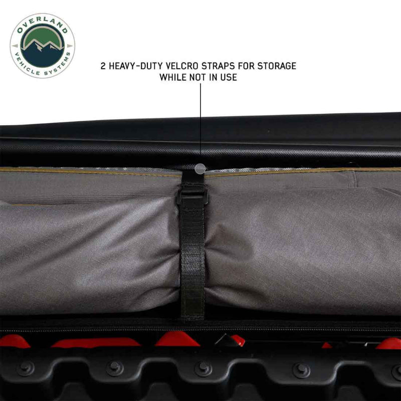 Image of a roof-mounted awning in stored position showing gray fabric securely rolled and held with heavy-duty Velcro storage straps, close-up exterior view on white background.