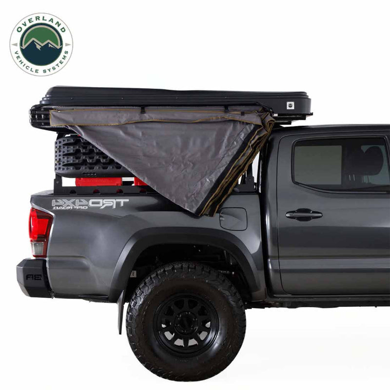 Image of a pickup truck with a roof-mounted 270-degree awning partially deployed, showing gray fabric folded outward from the side over the truck bed, side profile view on white background.