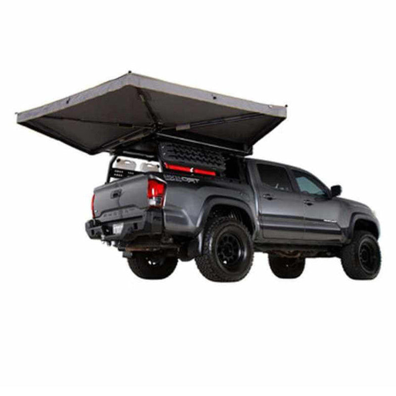 Image of a pickup truck with a roof-mounted awning fully deployed over the bed, gray fabric canopy with support arms, angled rear and side view on white background.
