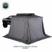 Image of Nomadic 270 LTE awning fully deployed with optional gray wall enclosure attached around a pickup truck, creating a tent-style privacy shelter, angled rear and side view on white background.