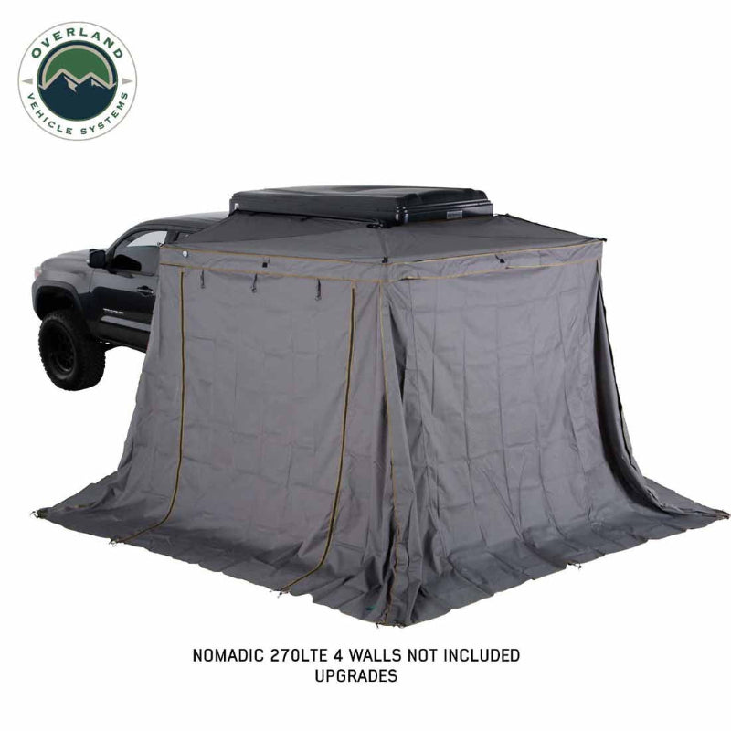 Image of Nomadic 270 LTE awning fully deployed with optional gray wall enclosure attached around a pickup truck, creating a tent-style privacy shelter, angled rear and side view on white background.