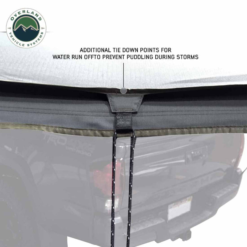 Image of a roof-mounted awning detail showing gray fabric edge with additional tie-down point and cord for water runoff control, close-up exterior view on white background.