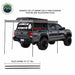 Image of a pickup truck with a roof-mounted 270-degree awning deployed using four telescoping support poles, gray fabric canopy extending along side and rear, angled rear and side view on white background.