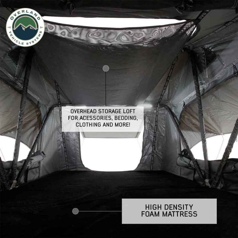 Image of the interior of an Overland Vehicle Systems Nomadic Standard rooftop tent, featuring a high-density foam mattress and an overhead storage loft for accessories, bedding, and clothing. A window is visible in the back, and the interior walls are grey