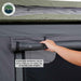 Image shows a hand rolling up the grey window flap of an Overland Vehicle Systems Nomadic Standard rooftop tent, revealing the black mesh screen underneath. The text highlights that the doors and windows can be easily rolled up using hook and loop straps