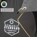 Image of a grey Overland Vehicle Systems Nomadic Standard awning, showing a gold support rod with a black capped end inserted into a silver grommet on the grey fabric. Text highlights "HEAVY DUTY RAIN FLY RODS WITH PROTECTIVE END CAPS AND WATER RUN OFF POINTS" and the awning features a white logo with "NOMADIC STANDARD 4 SEASONS READY