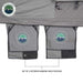 Image showcasing a pair of grey exterior hanging shoe pouches with the "Overland Vehicle Systems" mountain logo, positioned underneath a darker grey tent fabric. The "Overland Vehicle Systems" logo is in the top left corner