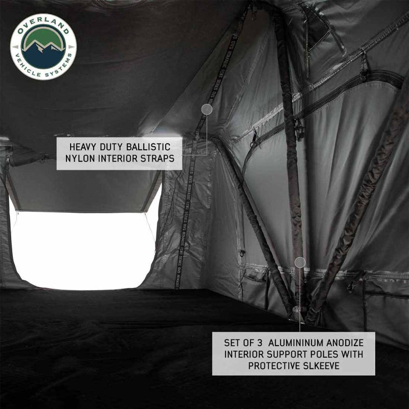 Image showcasing the interior of a dark grey rooftop tent, highlighting three aluminum anodized interior support poles with protective sleeves and heavy-duty ballistic nylon interior straps. The "Overland Vehicle Systems" logo is in the top left corner