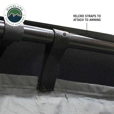 Image of a close-up of a vehicle awning room enclosure showing black Velcro straps wrapped around an awning support bar to attach the fabric panel, displayed in detail on a white background.