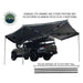 Image of a grey OVS Nomadic 270 Awning fully deployed with three telescoping aluminum poles extending to the ground for support. The awning is attached to the side of a black pickup truck with an overland rack and a rooftop tent. A graphic shows the extendable poles