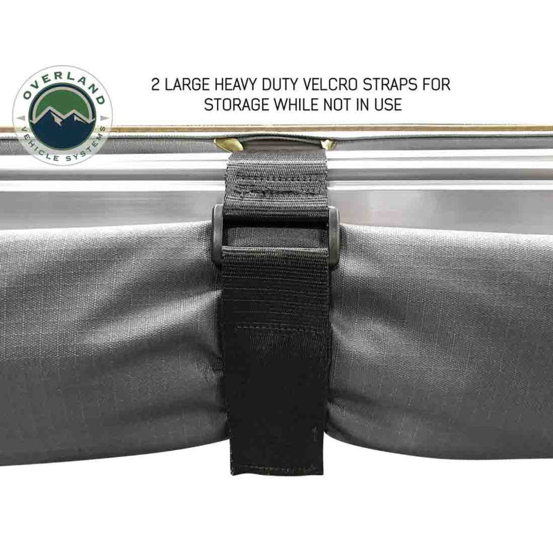 Image of the OVS Nomadic Awning rolled up and secured with a large heavy-duty Velcro strap for storage. The awning fabric is a dark grey color