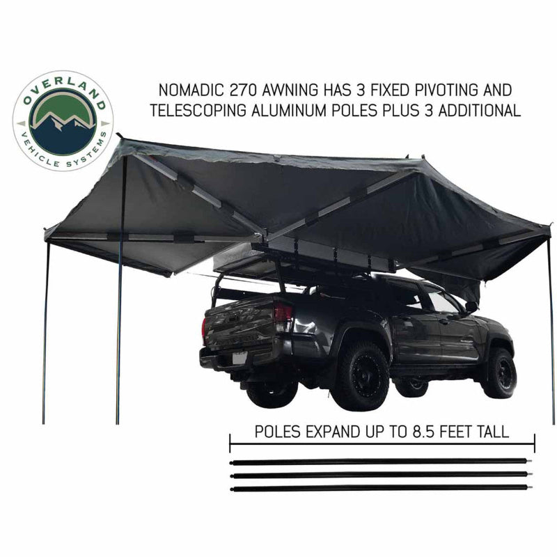 Image of the OVS Nomadic 270 Awning fully deployed on the side and rear of a grey truck, supported by telescoping aluminum poles. The awning is black on both sides