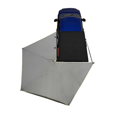 Image of an OVS HD Nomadic Awning, fully deployed in a U-shape around a blue vehicle, with a top-down view on a white background. The awning fabric is a light gray with black underside, and a black roof top tent is visible on the vehicle
