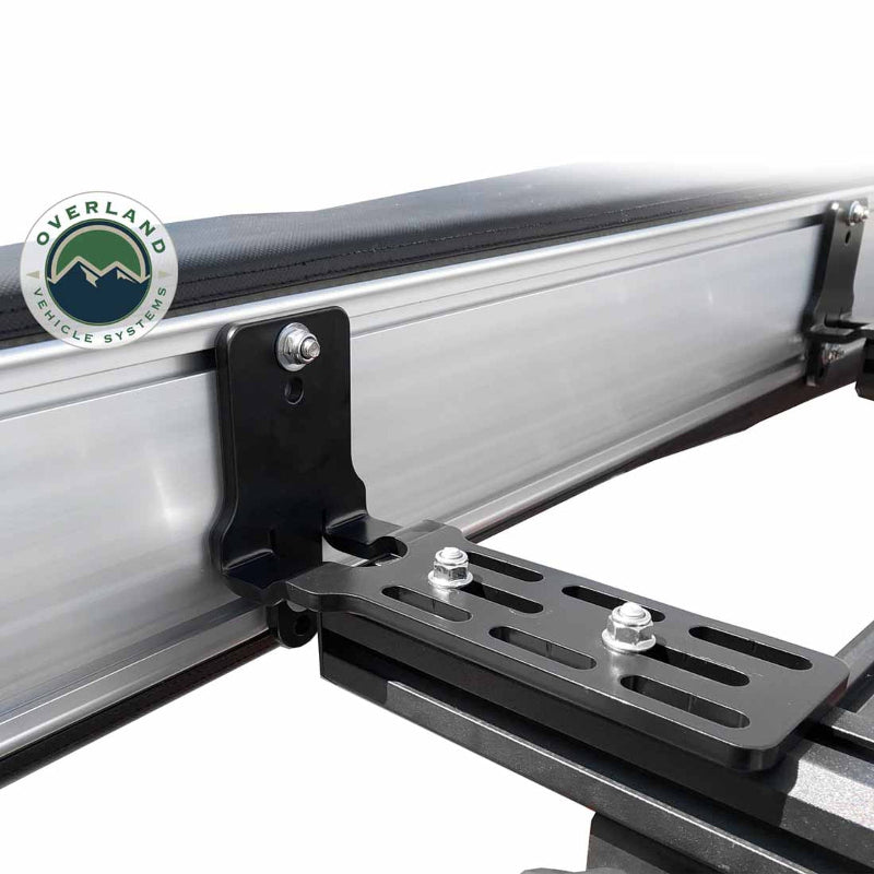 Image of the OVS Nomadic 180° Awning mounting brackets, including a black L-shaped bracket and a slotted flat bracket, shown in a close-up shot on a white background