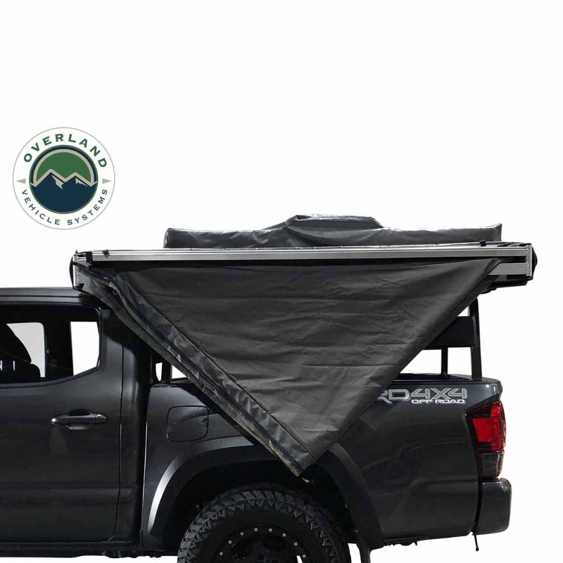 Image of the OVS Nomadic 180° Awning partially deployed on the side of a gray pickup truck, showcasing the black fabric with a side profile view on a white background