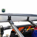 Image of a close-up of the mounting bracket for a rooftop tent or awning, attached to a roof rack. An orange traction board, a shovel, and other off-road accessories are visible underneath