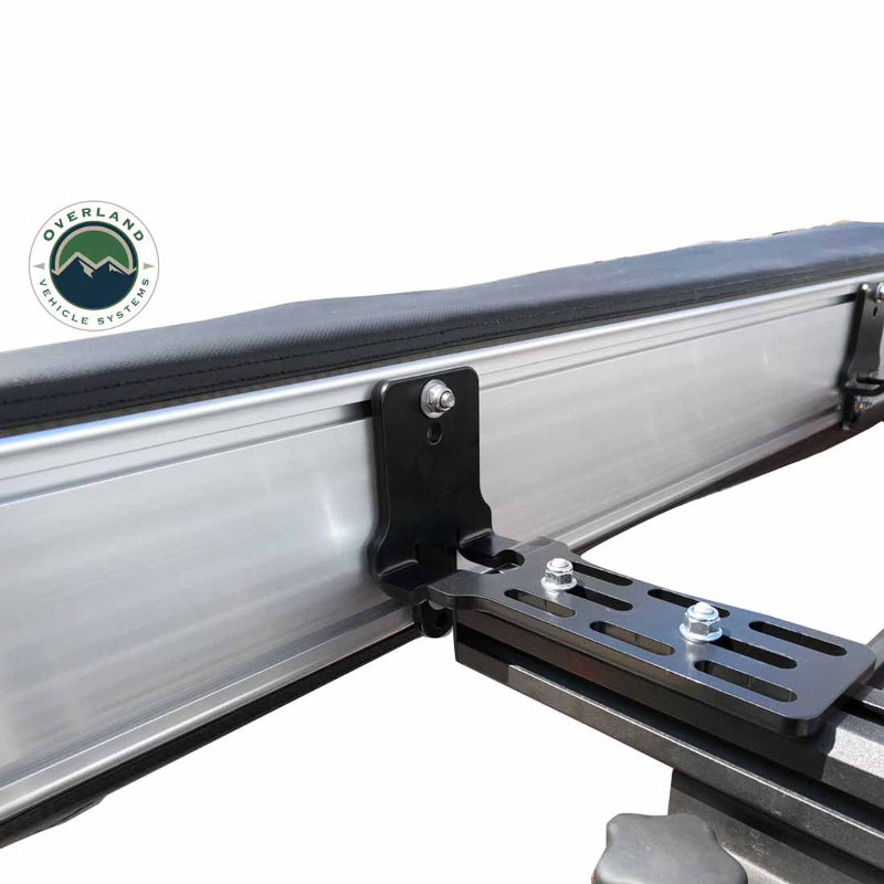 Image of a black mounting bracket securing a rooftop tent or awning to a roof rack. The bracket is attached with two bolts, shown against a white background with the Overland Vehicle Systems logo in the top left corner