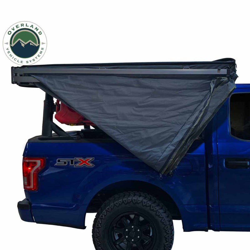 Image of a blue pickup truck with a black rooftop tent and a gray awning partially deployed over the truck bed. The Overland Vehicle Systems logo is visible in the top left, with a white background