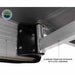 Image of a close-up of the black hinged bracket of an awning attached to the aluminum frame. Text labels the "ALUMINUM FRAME BOX EXTRUSION WITH STEEL HARDWARE" with arrows pointing to the corresponding parts