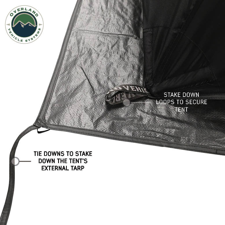 Image of OVS hub-style camping tent base detail showing stake-down loops and tie-down straps for securing the external tarp, black and gray fabric, close-up angled view on a white background.