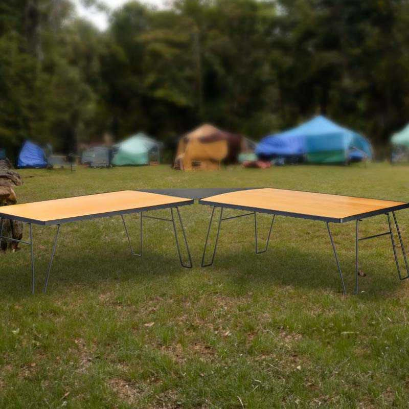 Image of modular camping tables connected together, bamboo wood tabletops with black metal folding legs, outdoor campsite setting with tents in background, angled front view.