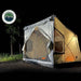 A lit-up OVS ground tent is set up at night in a wooded area. The interior lights illuminate the tent, showcasing the mesh windows and the gray fabric