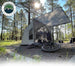 An angled front view of the OVS ground tent shows it deployed in a forest campsite with an awning providing shade. A mountain bike is leaning against the tent, set on a gravel pad with trees in the background and sunlight shining down