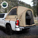 Image of a pickup truck bed tent installed on a white truck, tan fabric with mesh windows and open rear entry, angled rear and side view in an outdoor mountain setting.