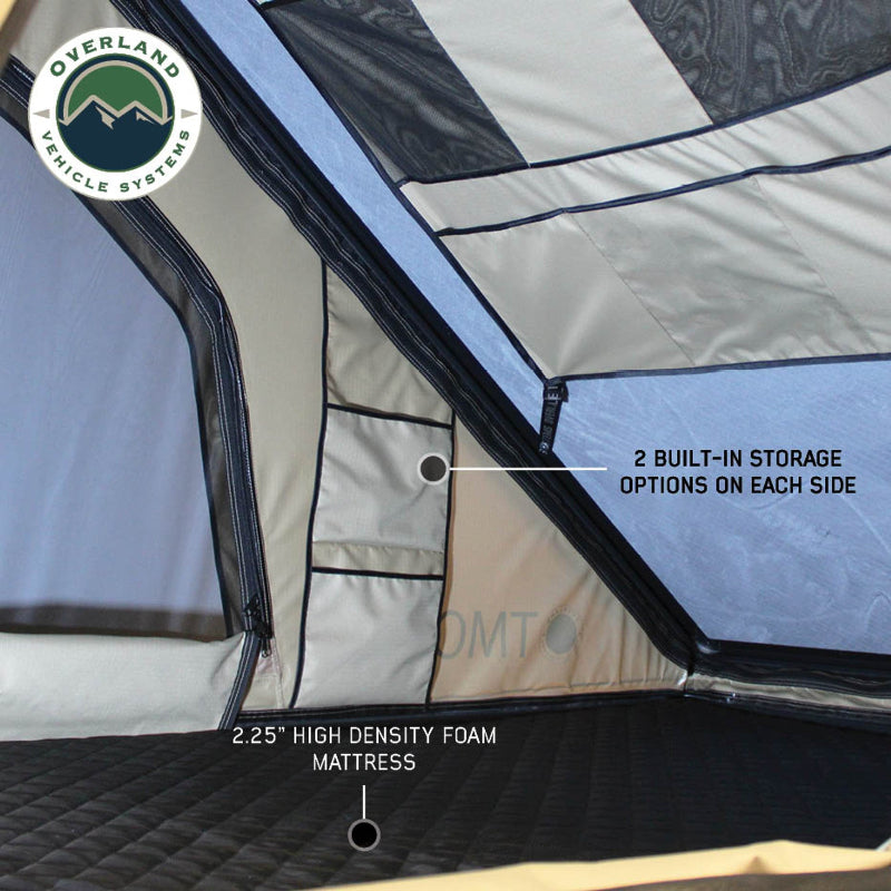 Image of the interior of an Overland Vehicle Systems tent, showcasing overhead storage options with mesh pockets and beige fabric compartments. The tent also features 2.25" high density foam mattress and two built-in storage options on each side