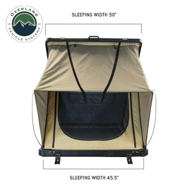 Image of a beige Overland Vehicle Systems rooftop tent, fully deployed with a ladder extending to the ground, against a white background. The tent features a prominent "TMON" logo on its side